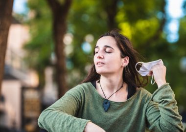 Young woman removes mask from her face with relief before the end of the pandemic